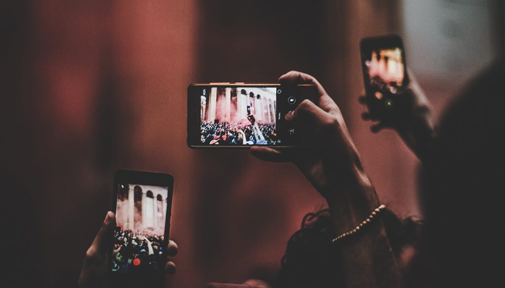 photo of multiple people holding up phones to take a photo.